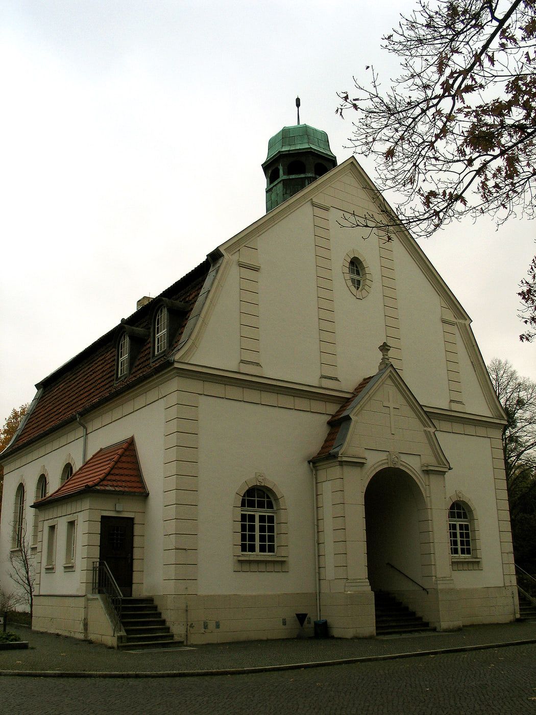 Alte Kapelle mit heller Fassade und grünem Dachreiter zwischen kahlen Bäumen auf Stadtfriedhof Ricklingen