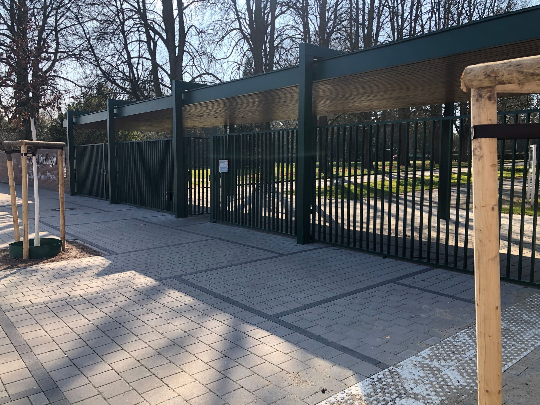 Moderner Eingang mit schwarzem Gittertor und jungen Straßenbäumen auf Stadtfriedhof Ricklingen